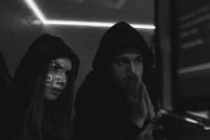 Two people in hoodies sitting in front of a computer screen, representing hackers in a dark room.